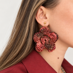 Raffia flower statement earring in warm red and brown tones worn on the ear with a gold-tone fastening