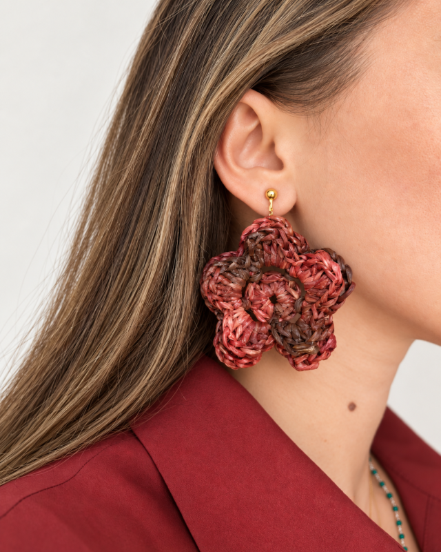 Raffia flower statement earring in warm red and brown tones worn on the ear with a gold-tone fastening