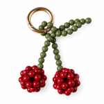 Burgundy beaded cherry bag charm with olive-green stems and a gold-tone ring on a white background.