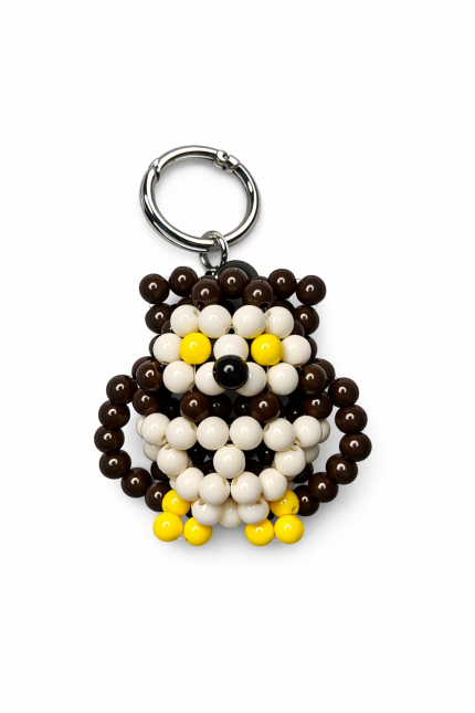 Brown and ivory beaded owl bag charm with yellow details and a silver-tone ring on a white background
