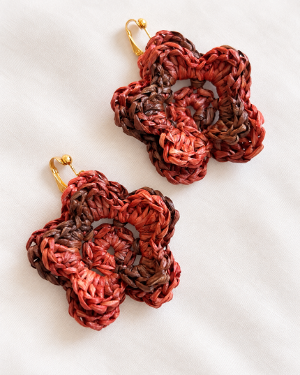 Pair of red and brown raffia flower clip-on earrings with gold-tone fastenings on a light fabric background