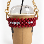Burgundy LOVE IT beaded cup carrier with a gold-tone chain holding a takeaway coffee cup