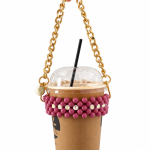 Hand holding a takeaway coffee cup in a dusty pink MUST HAVE beaded carrier with a gold-tone chain